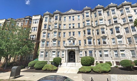 A large, multi-story building with a central entrance and a row of bushes in front.