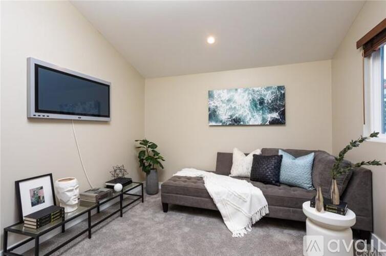 A living room with a grey couch, a television, a plant, and a painting on the wall.