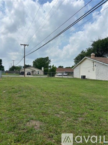 A grassy field with a house and power lines in the background.