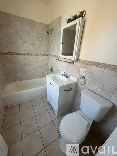 A white toilet sits next to a bathtub in a tiled bathroom.