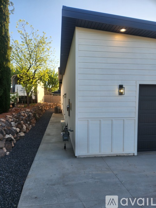 A white house with a black garage door and a stone wall.