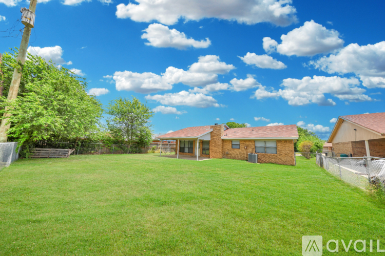 A grassy yard with a house and a fence in the background.