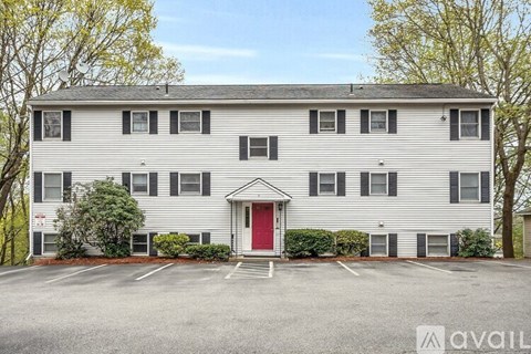 A two-story building with a red door and a parking lot in front.