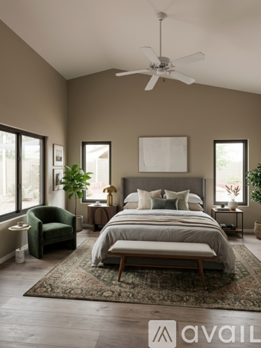 A bedroom with a large bed, a green armchair, and a ceiling fan.