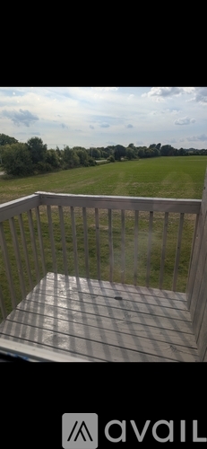 A balcony with a wooden railing and a bench overlooking a green field.