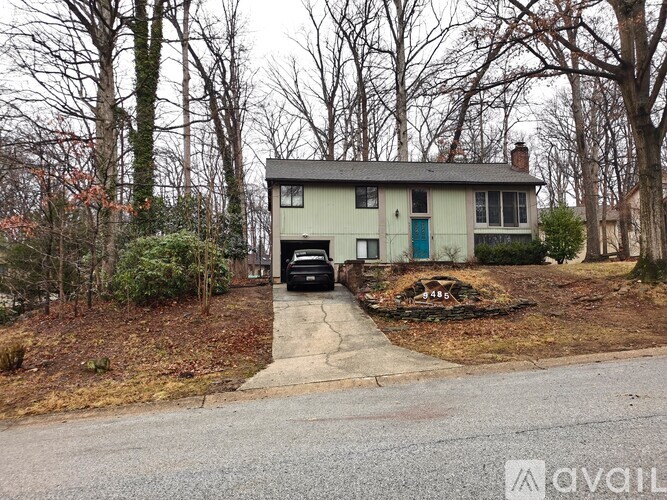 A house with a blue door is surrounded by trees and has a car parked in the driveway.