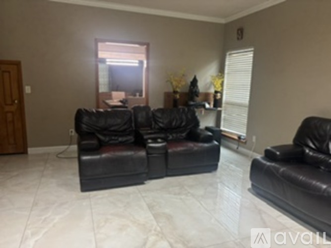 A black leather couch in a living room with a window behind it.
