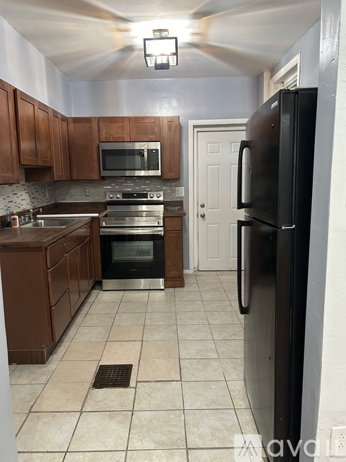 A kitchen with a black refrigerator, brown cabinets, and a white door.