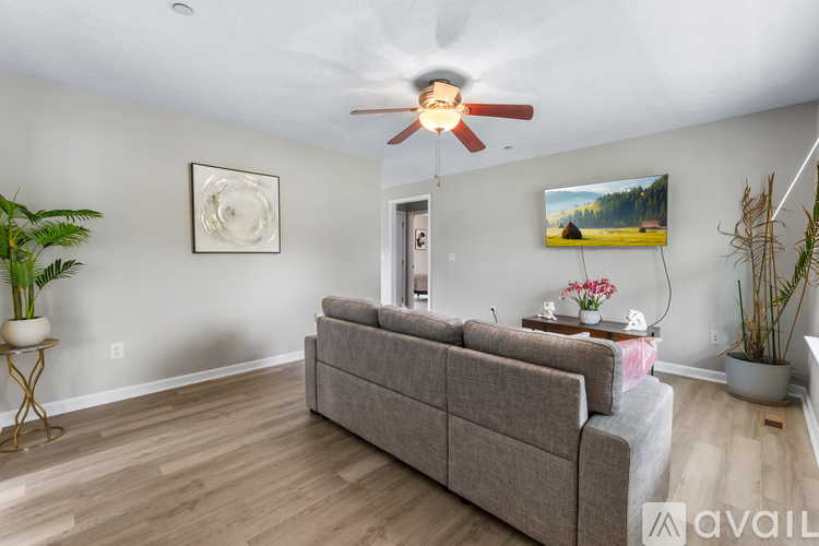 A living room with a grey couch, a ceiling fan, and a painting on the wall.