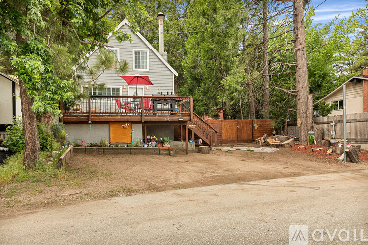 A house with a grey exterior and a red awning is surrounded by trees and has a wooden deck.