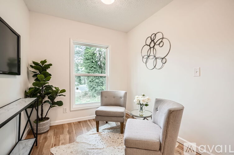 A living room with a grey couch, a white chair, a small table with a vase of flowers, and a television.