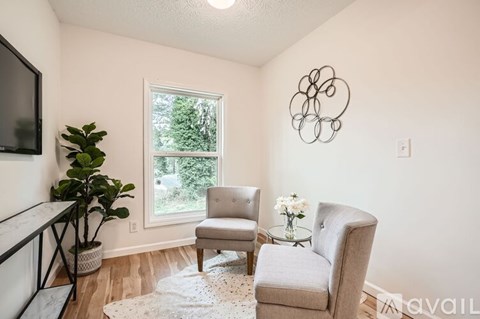 A living room with a grey couch, a white chair, a small table with a vase of flowers, and a television.
