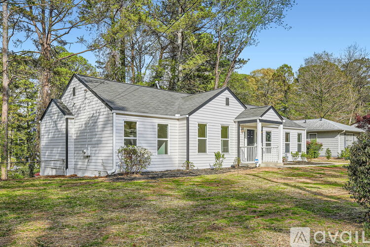 A house with a grey roof and white walls is surrounded by trees.