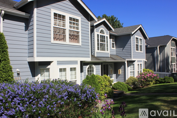 A house with a blue exterior and white trim is surrounded by a well-manicured lawn and vibrant flowers.
