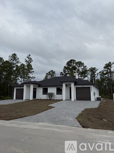 A house with a grey roof and white walls is surrounded by trees.