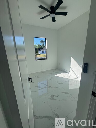 A room with a ceiling fan and a window overlooking a house.