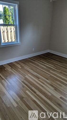 A room with wooden flooring and a window with a view of trees.