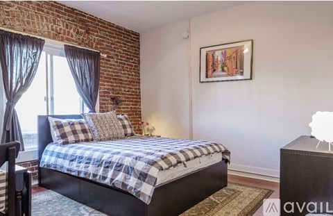 A bedroom with a brick wall and a bed with a plaid comforter.