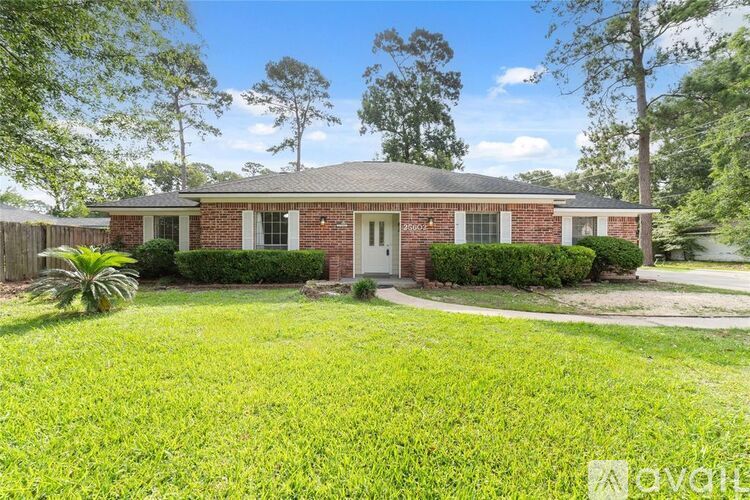 A house with a red brick exterior and a white door is surrounded by greenery.