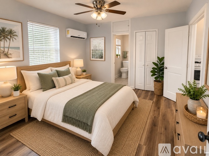 A bedroom with a large bed, a ceiling fan, and a view of the beach through the window.
