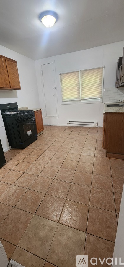 A kitchen with a black stove top oven and brown tile flooring.