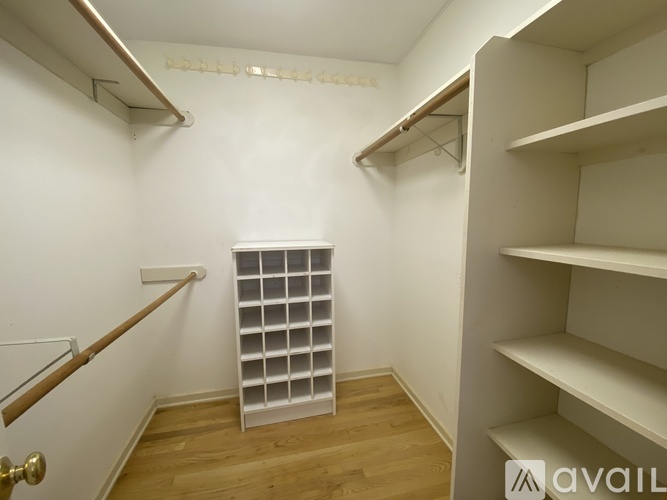 A white walk-in closet with shelves and a wooden floor.