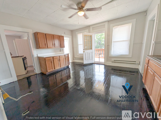 A spacious empty room with a ceiling fan and wooden cabinets.
