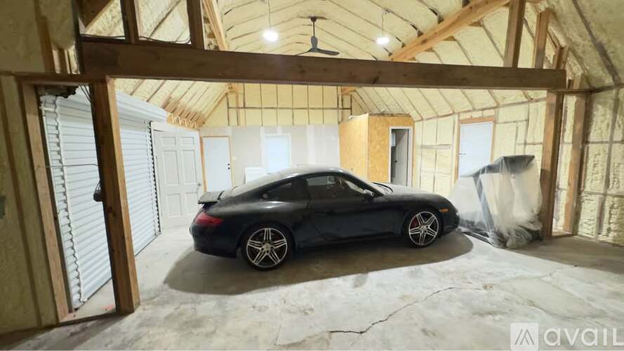 A black car is parked inside a garage under construction.