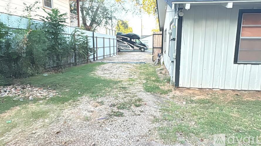 A gravel path leads to a white building with a black car parked in the driveway.