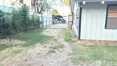 A gravel path leads to a white building with a black car parked in the driveway.