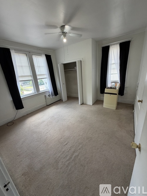 A room with a carpeted floor, a ceiling fan, and a window with black curtains.
