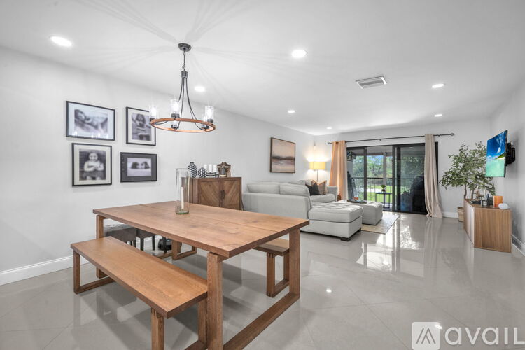 A modern dining room with a wooden table and bench, a chandelier, and framed pictures on the wall.