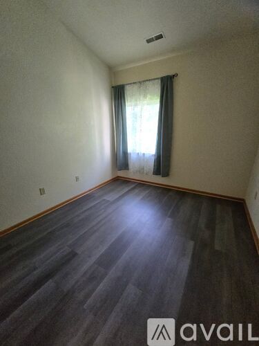 A room with wooden flooring and a window with curtains.