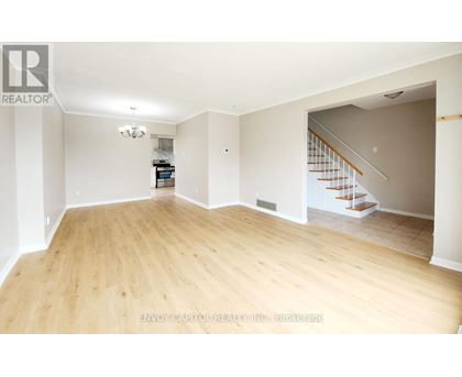 A spacious room with wooden flooring and a staircase in the background.