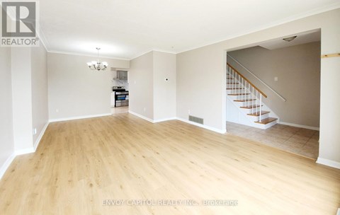 A spacious room with wooden flooring and a staircase in the background.