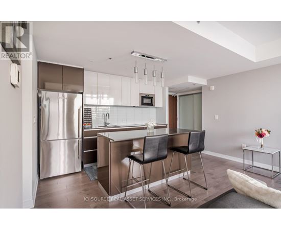 A modern kitchen with a refrigerator, sink, and bar stools.