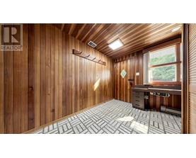 A room with wooden walls and ceiling, a desk with a computer, and a window with a view of trees.
