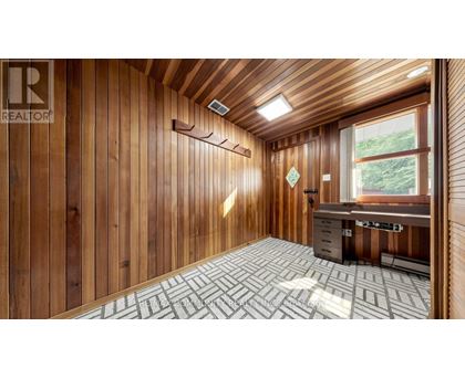 A room with wooden walls and ceiling, a desk with a computer, and a window with a view of trees.