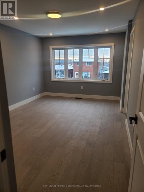 A room with wooden flooring and a window showing a view of a red building.