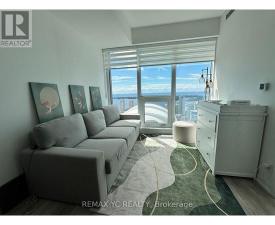 A living room with a grey couch and a large window overlooking the city.