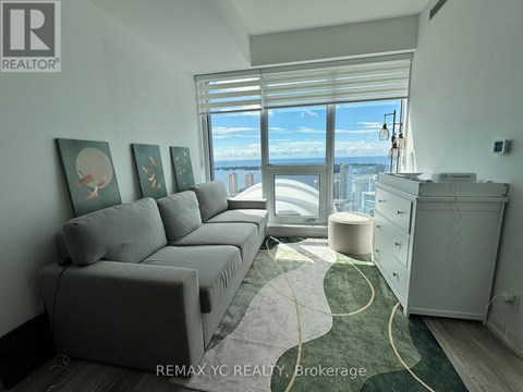 A living room with a grey couch and a large window overlooking the city.