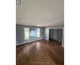 A room with wooden flooring and a window showing a view of trees and a road.