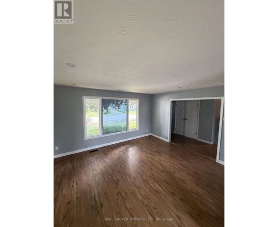 A room with wooden flooring and a window showing a view of trees and a road.