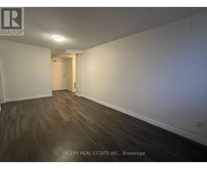 A room with wooden flooring and white walls, part of a property managed by Valery Real Estate Inc.