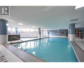 A swimming pool inside a building with a bench and a diving board.