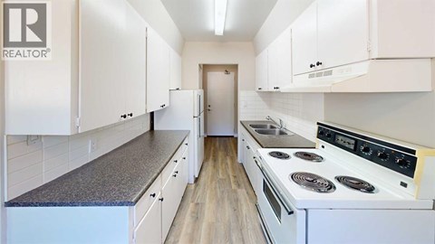 A white kitchen with a stove top oven and cabinets.
