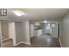 A well-lit, spacious kitchen and living room area with a refrigerator, sink, and cabinets.