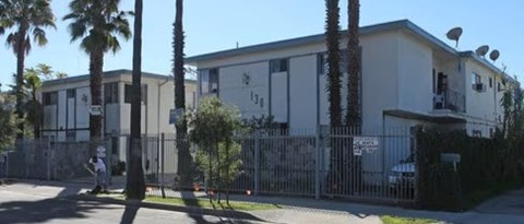 A white building with a black fence and palm trees in front.