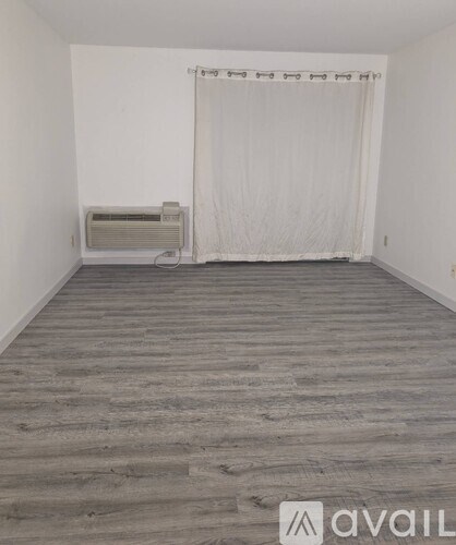 A room with wooden flooring and a window with curtains.