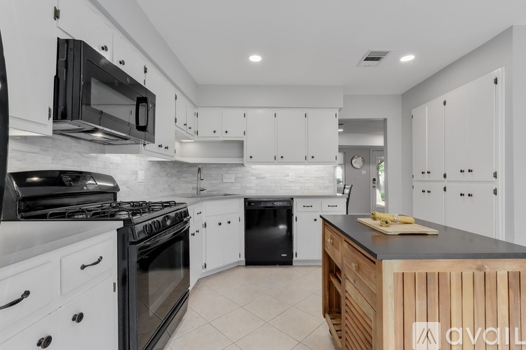 A modern kitchen with white cabinets and black appliances.